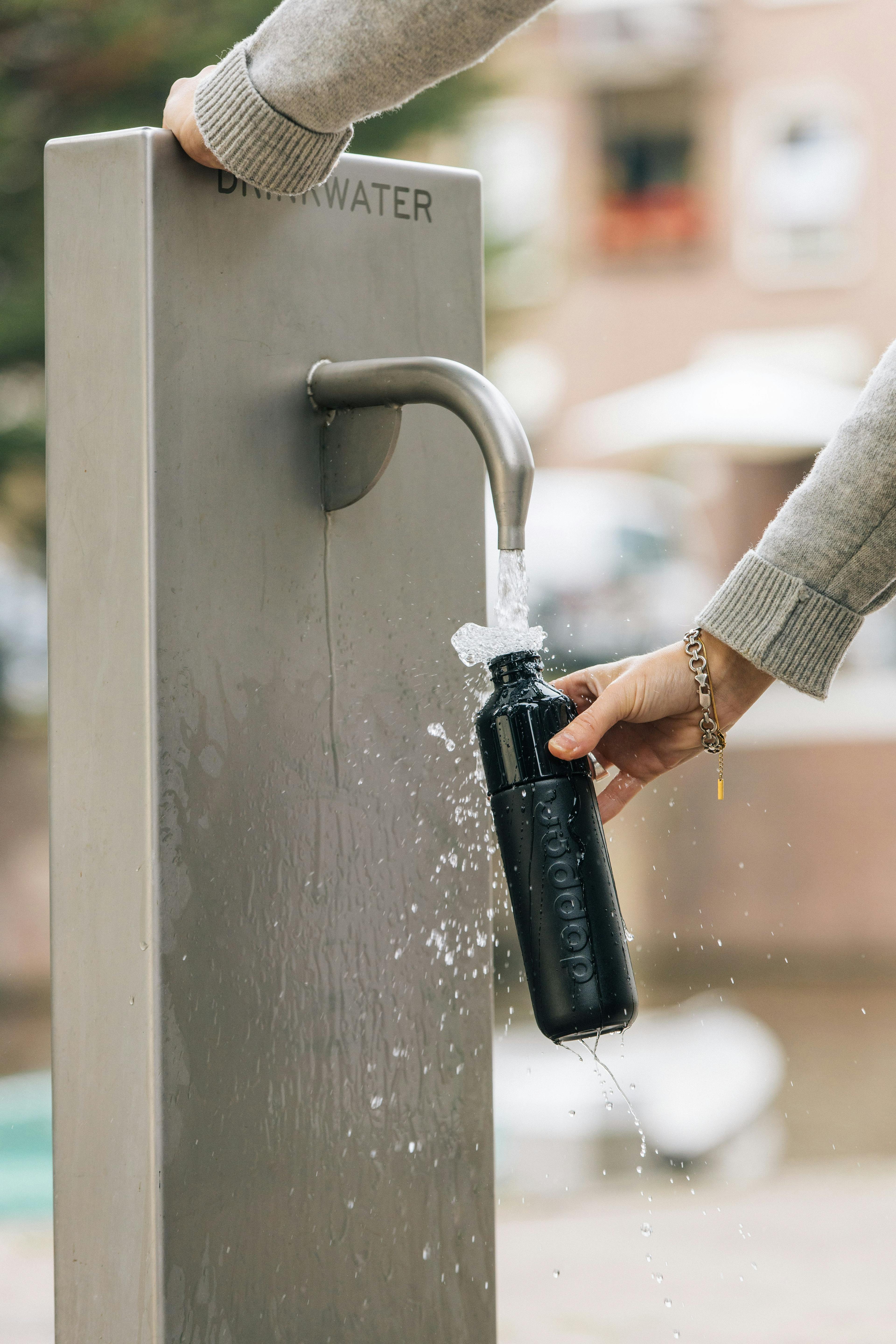 Person refilling their black Dopper bottle at a public water tap