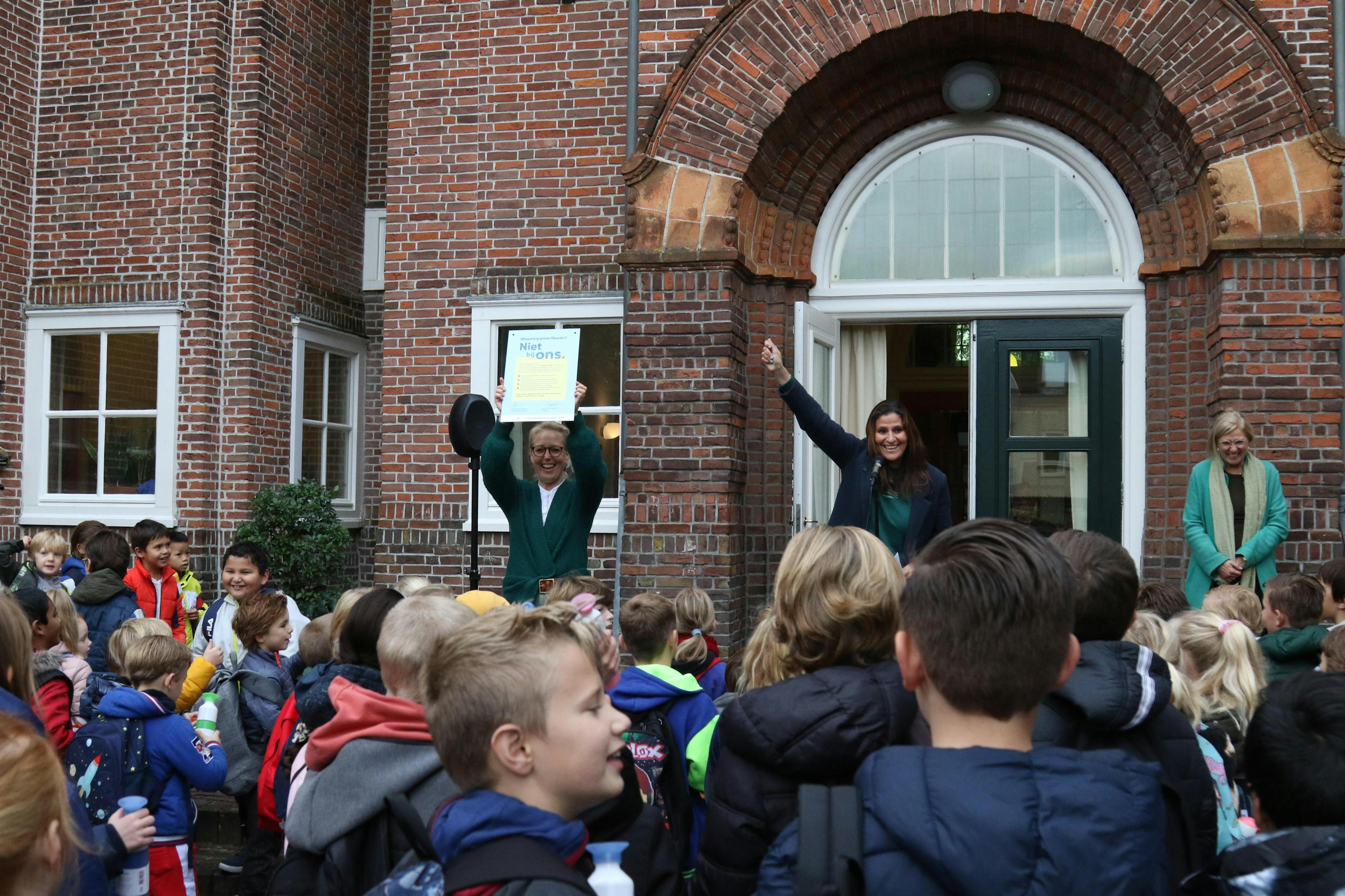 People and kids in front of a school holding up the Dopper Wave sign